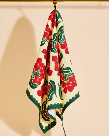 A cream-colored scarf with a bold red floral and green leaf pattern, hanging from a gold rod against a warm beige background.