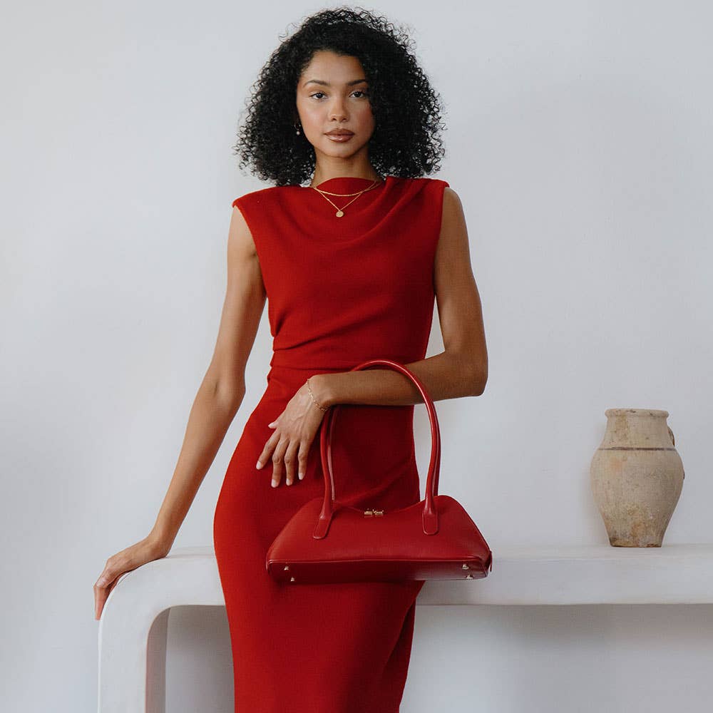 Woman in a red dress holding a matching red handbag against a white background