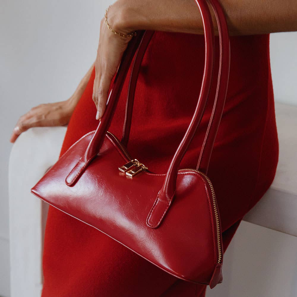 Red handbag held by a person wearing a red dress against a neutral background