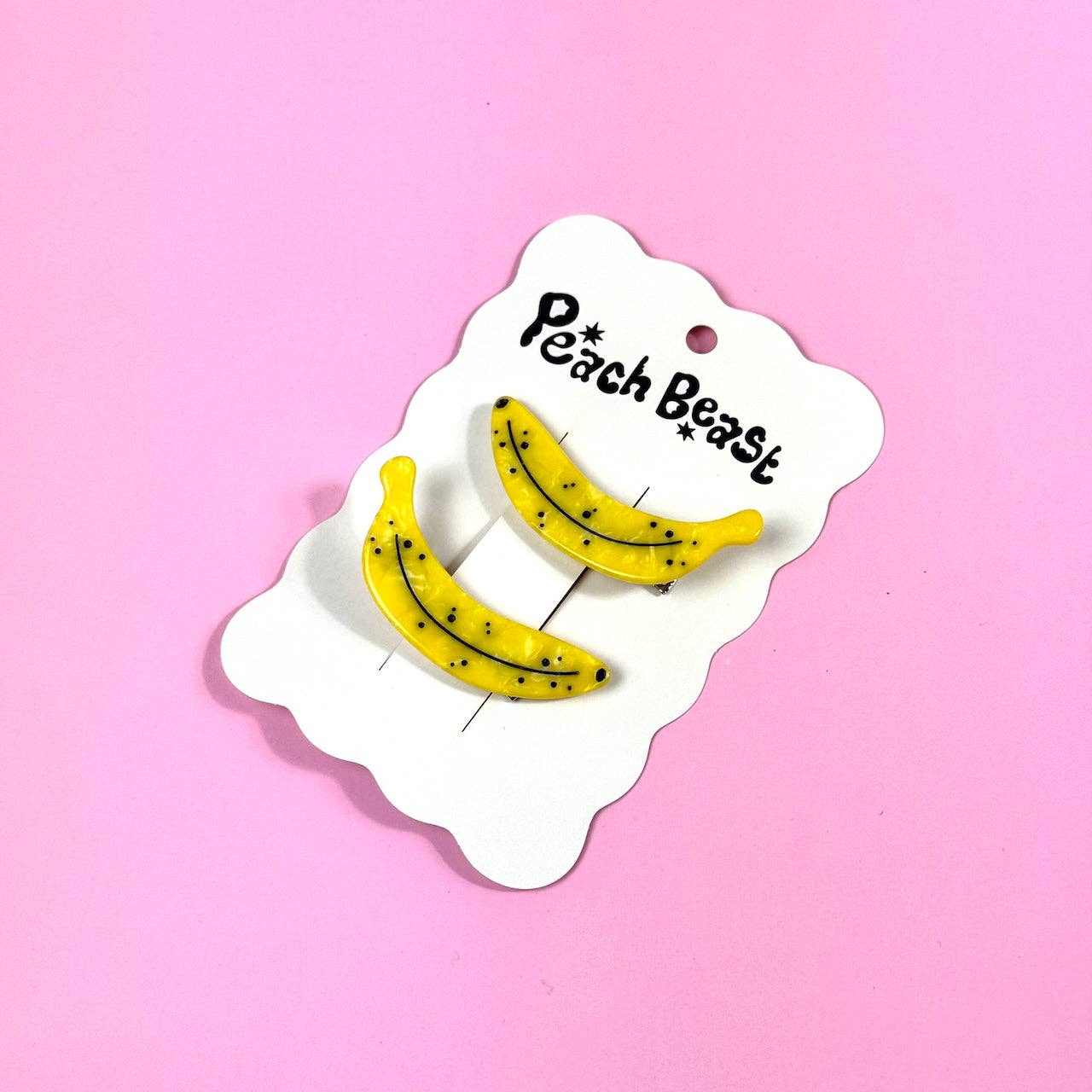Yellow banana-shaped hair clips on a 'Peach Beast' branded card against a pink background