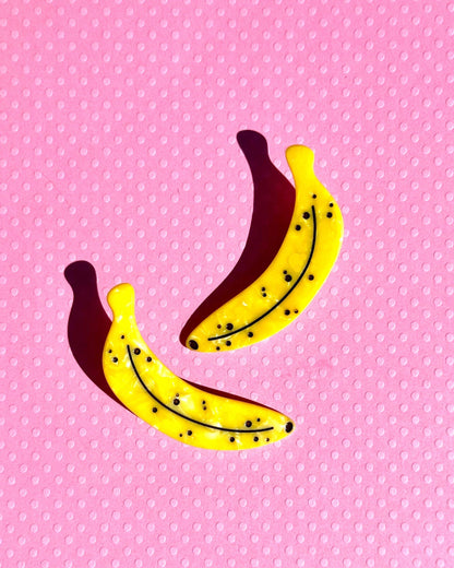 Two banana hair clips on a pink polka dot background