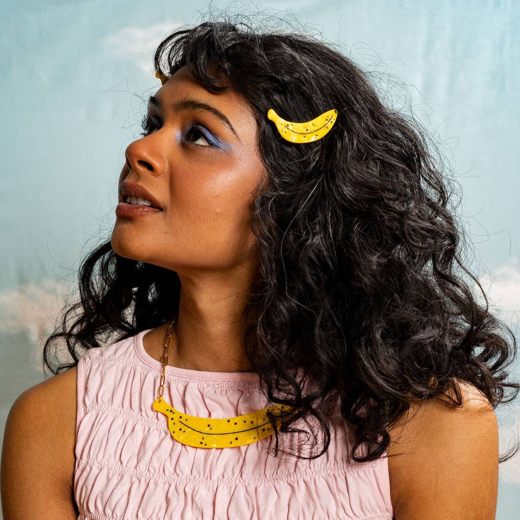 Woman with curly hair wearing yellow banana hair clips against a light blue background