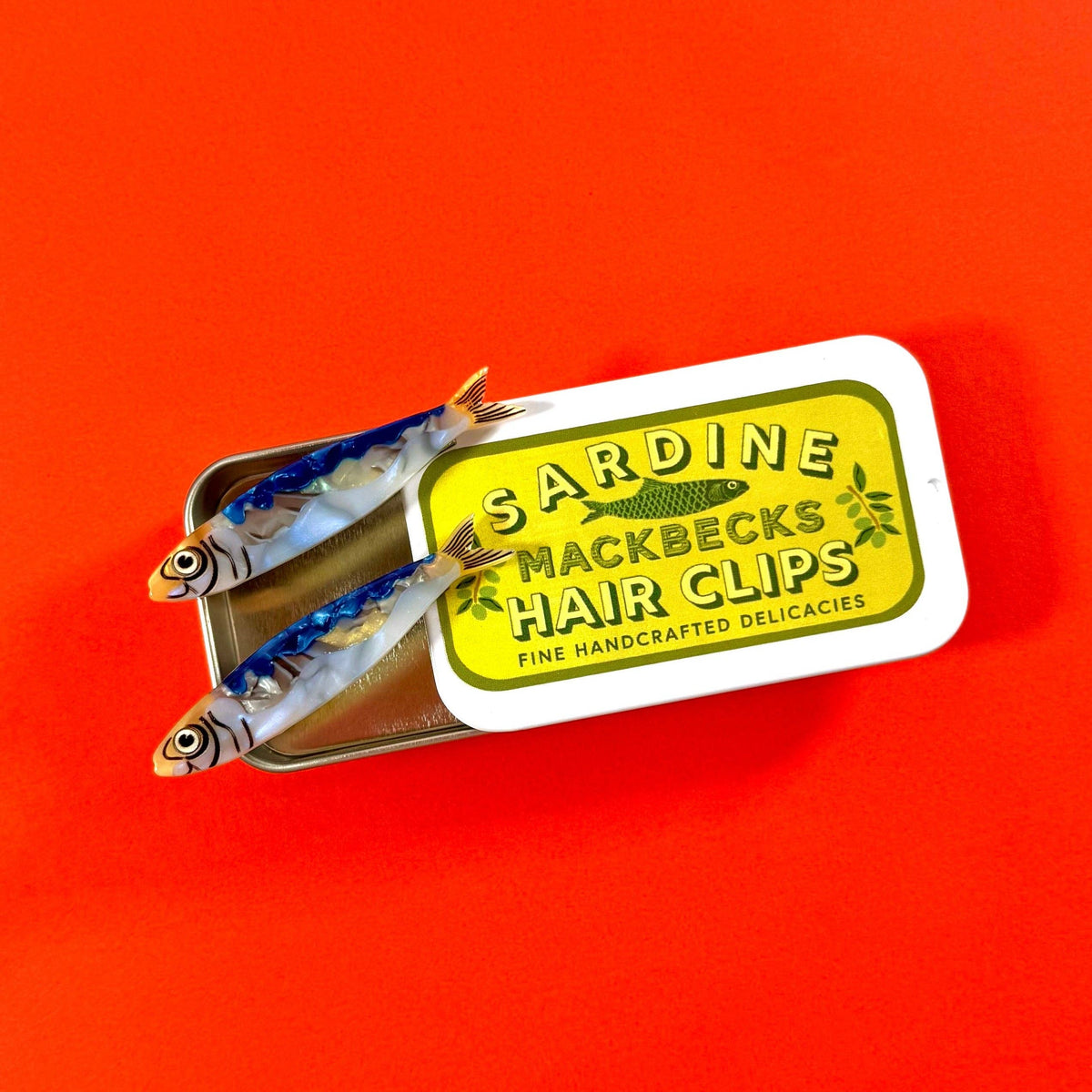 Sardine-shaped hair clips with a label on an orange background