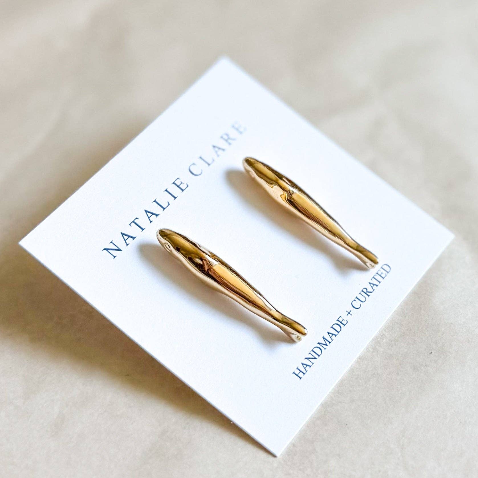 Gold earrings on a white card with 'Natalie Clare' branding.
