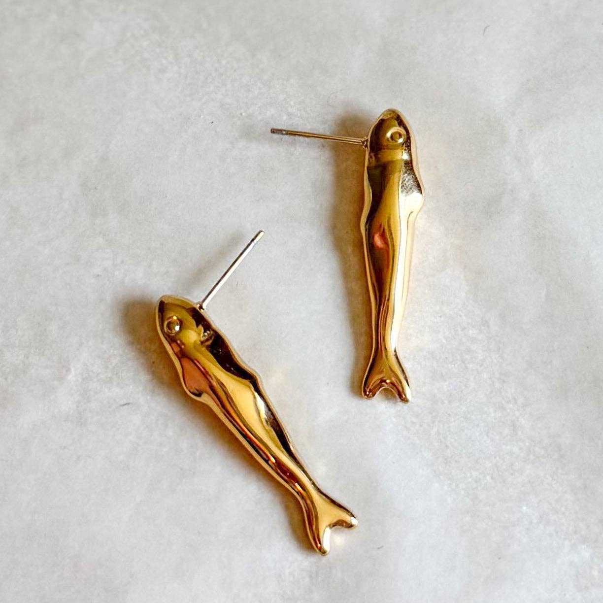 Gold fish-shaped earrings on a light gray background