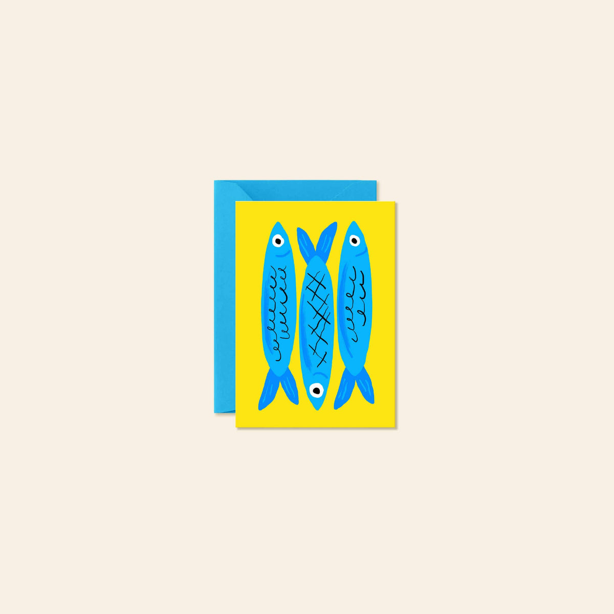 A greeting card featuring three stylized blue fish on a bright yellow background, shown with a blue envelope behind it on a light beige background.