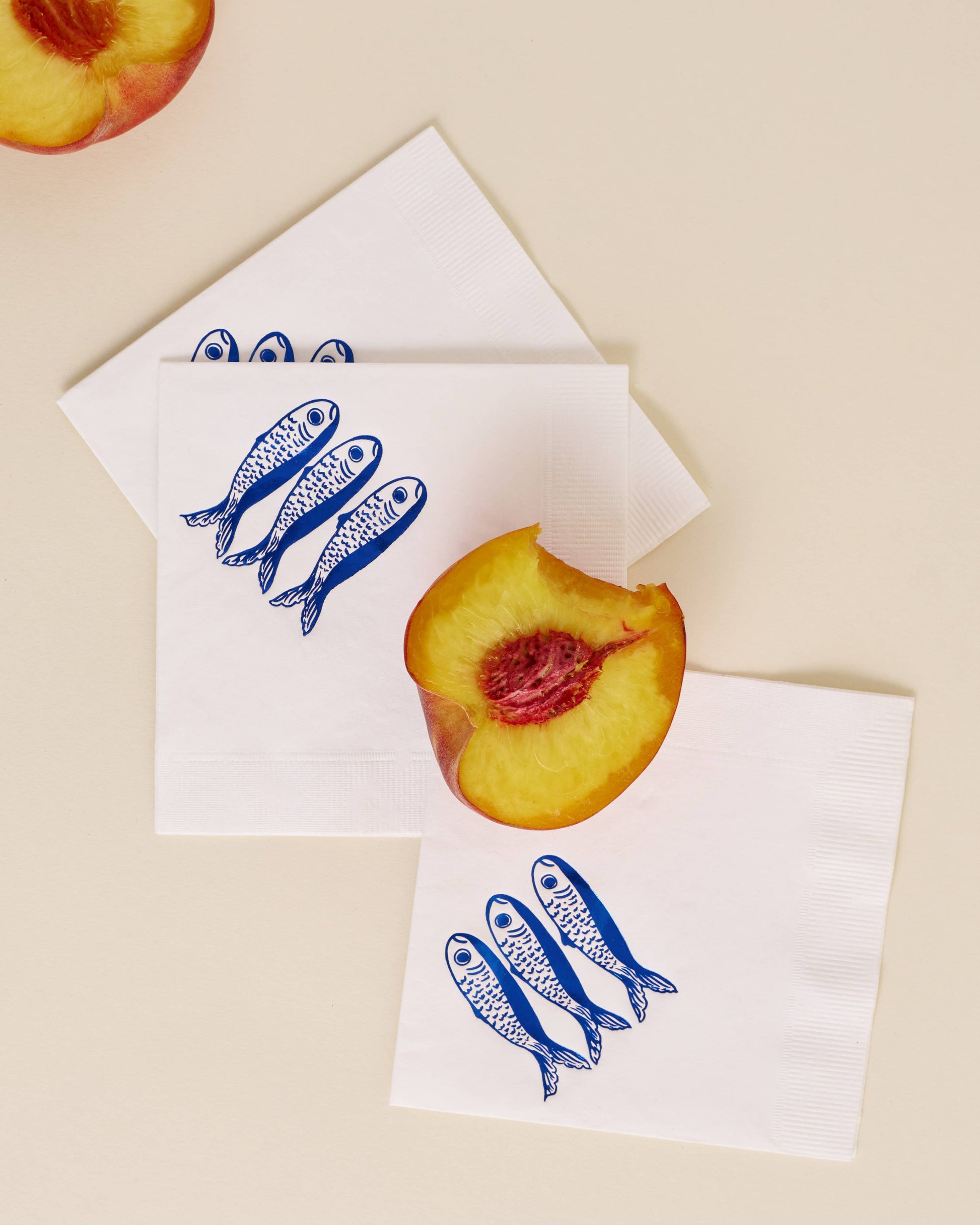 Two white napkins with blue fish design and peach slices on a beige background