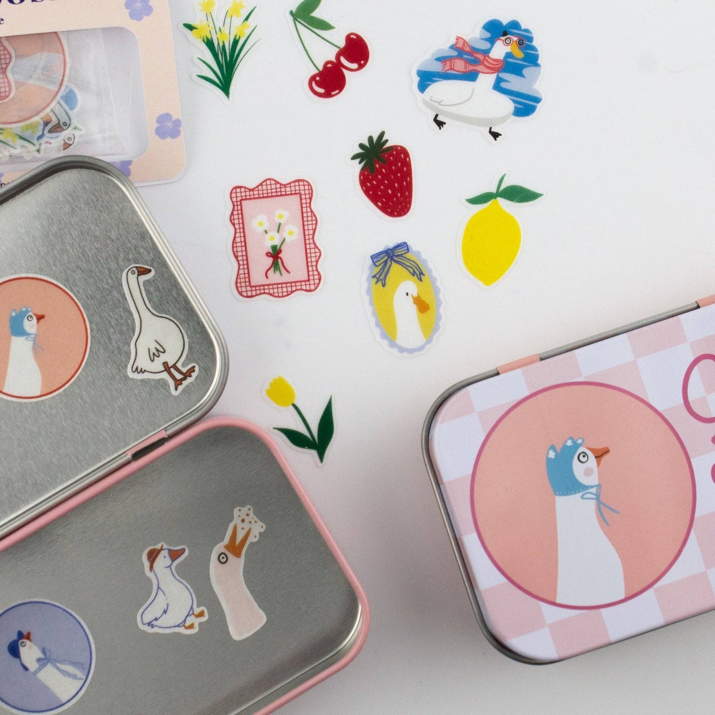 Decorative tins with cartoon penguin design and scattered stickers on a white background