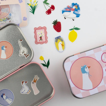 Decorative tins with cartoon penguin design and scattered stickers on a white background