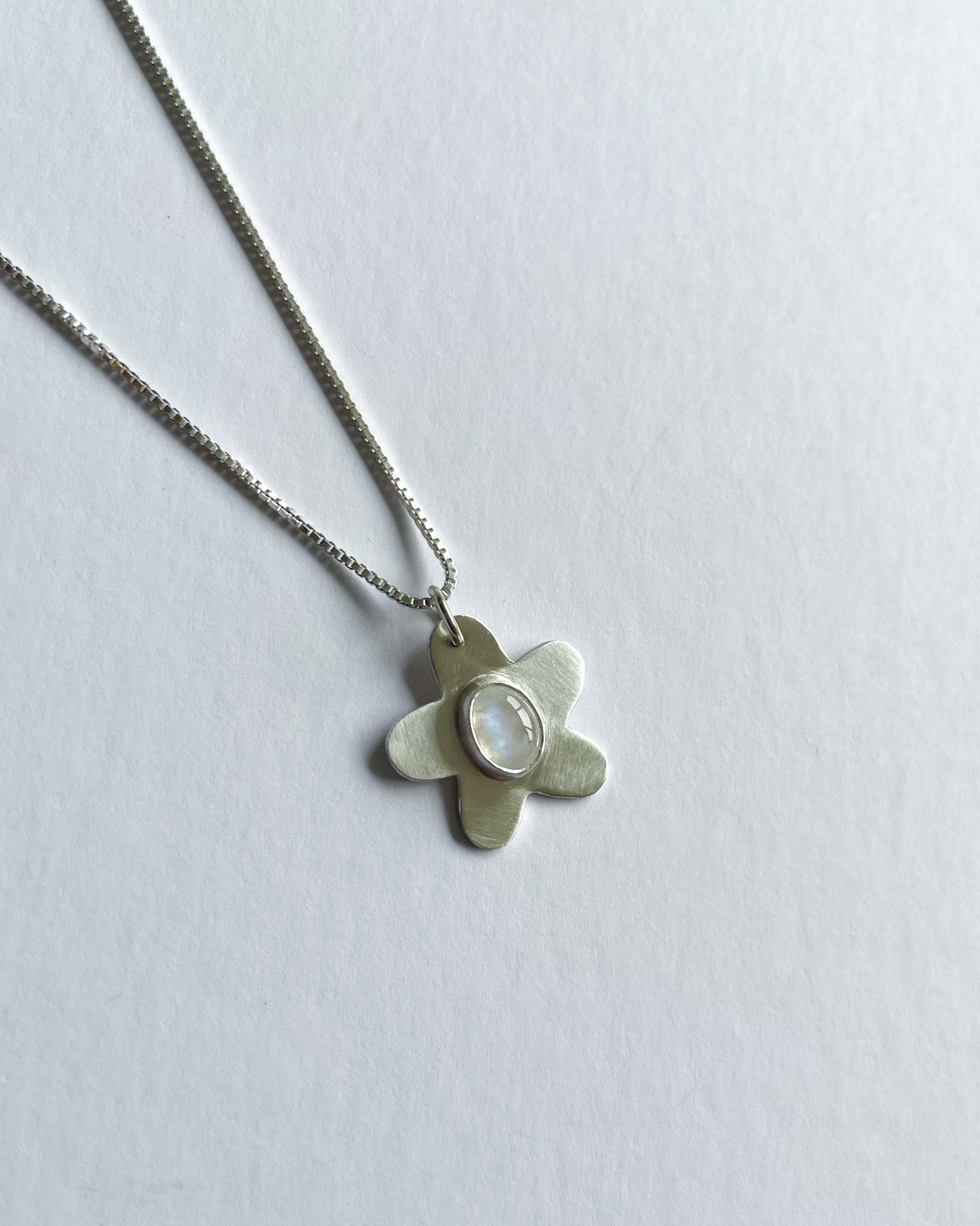 Silver necklace with a flower pendant on a light gray background