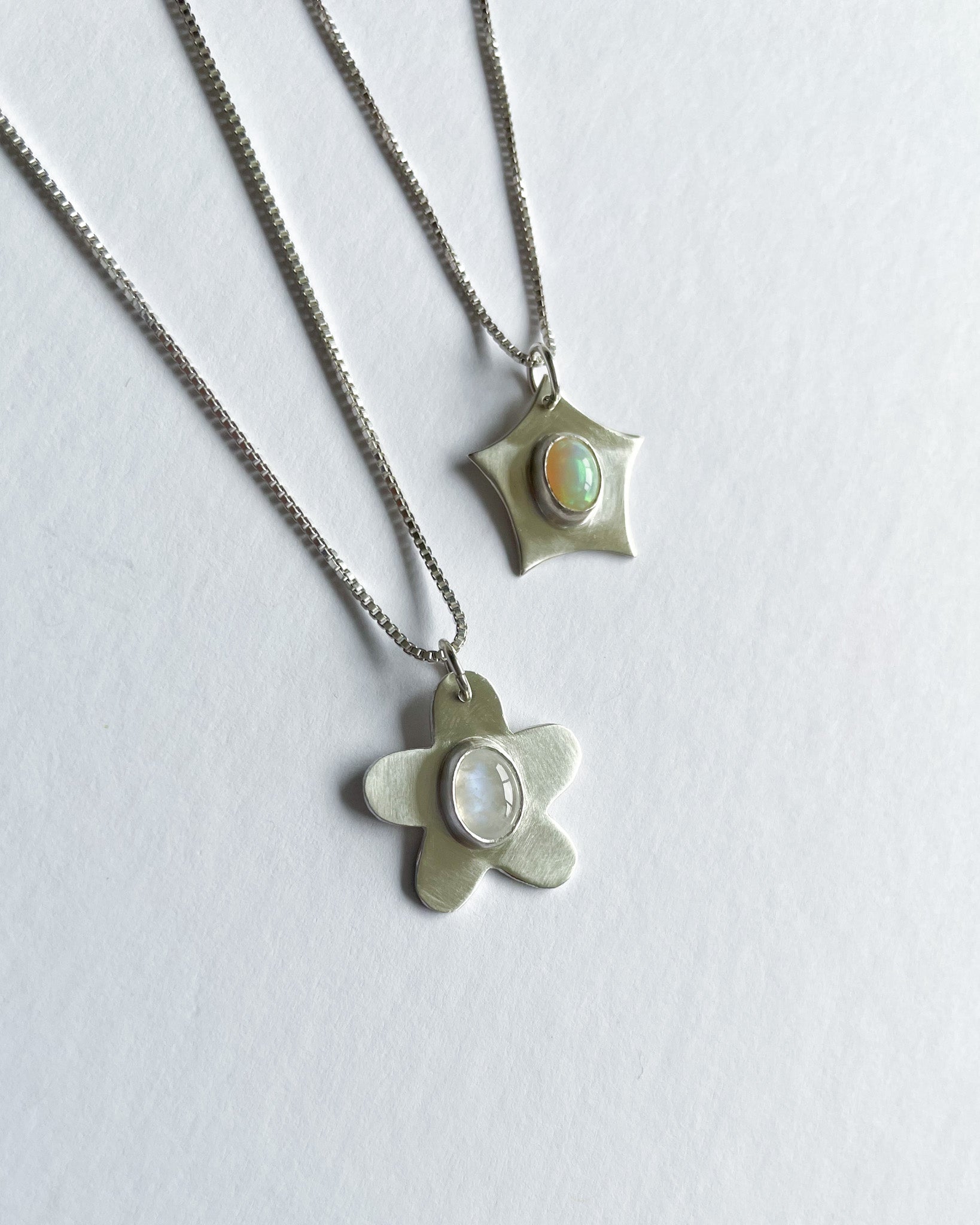 Two silver pendants with opal stones on a white background