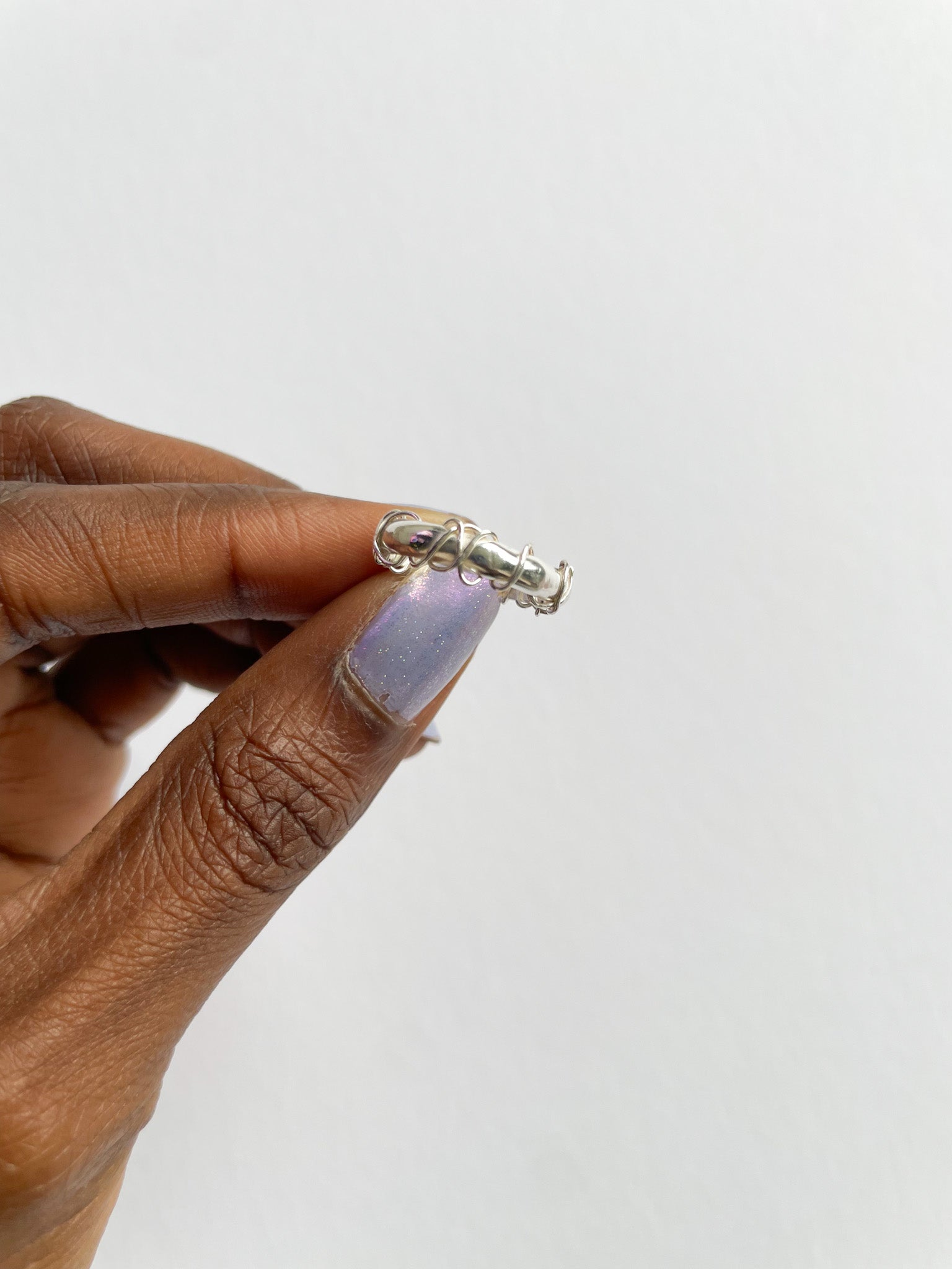 Hand holding a silver ring with a purple gemstone against a white background