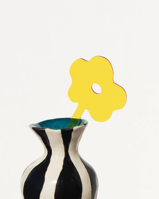 Black and white striped vase with a yellow flower-shaped object on a white background
