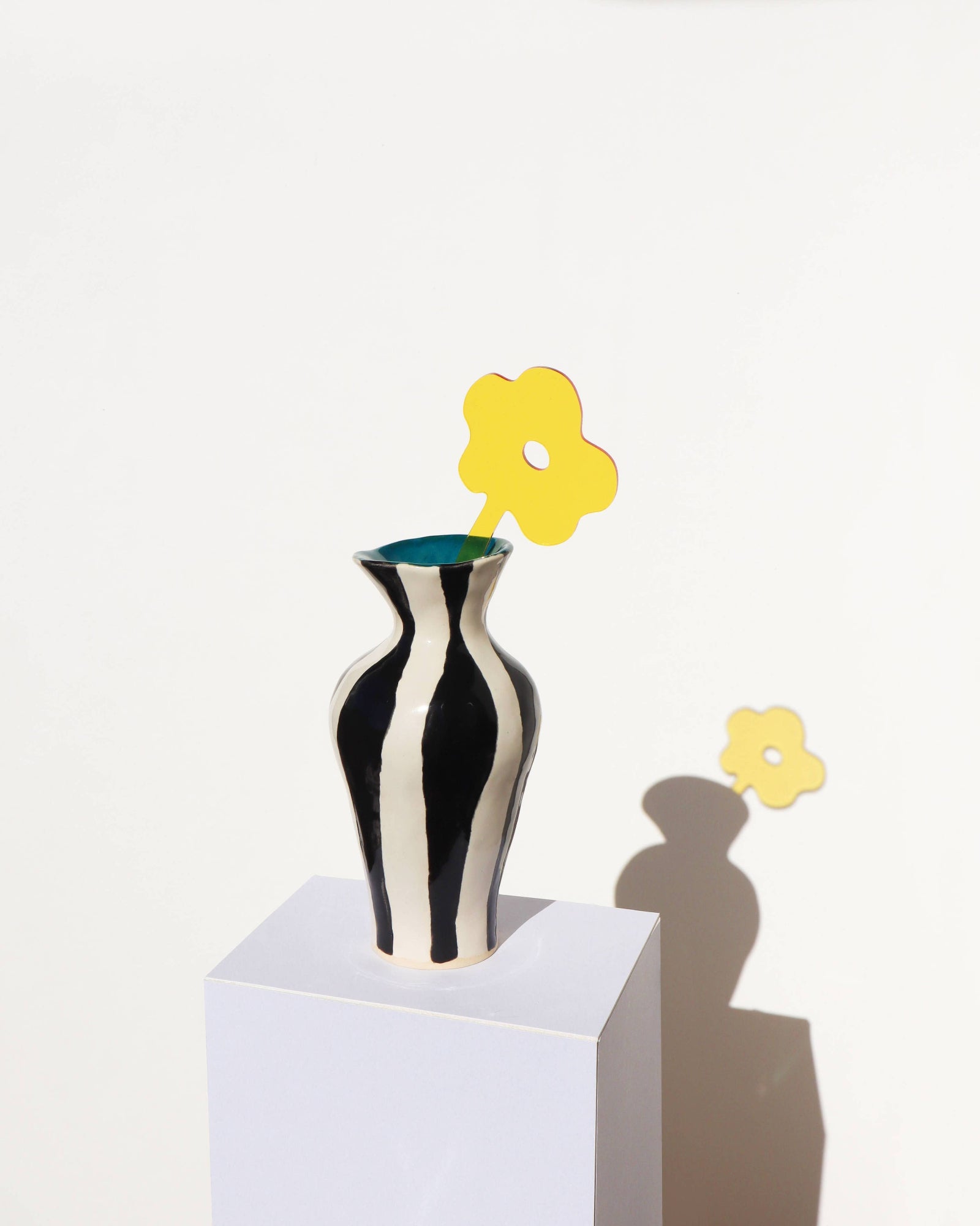 Black and white striped vase with yellow flowers on a white background