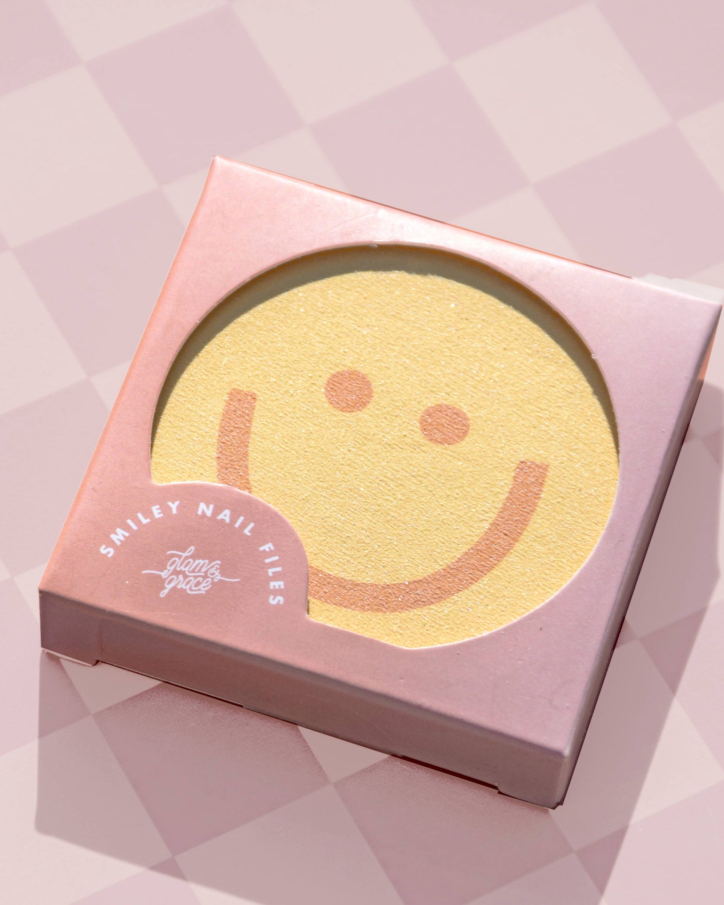 Smiley face nail file in a pink box on a pink geometric patterned background