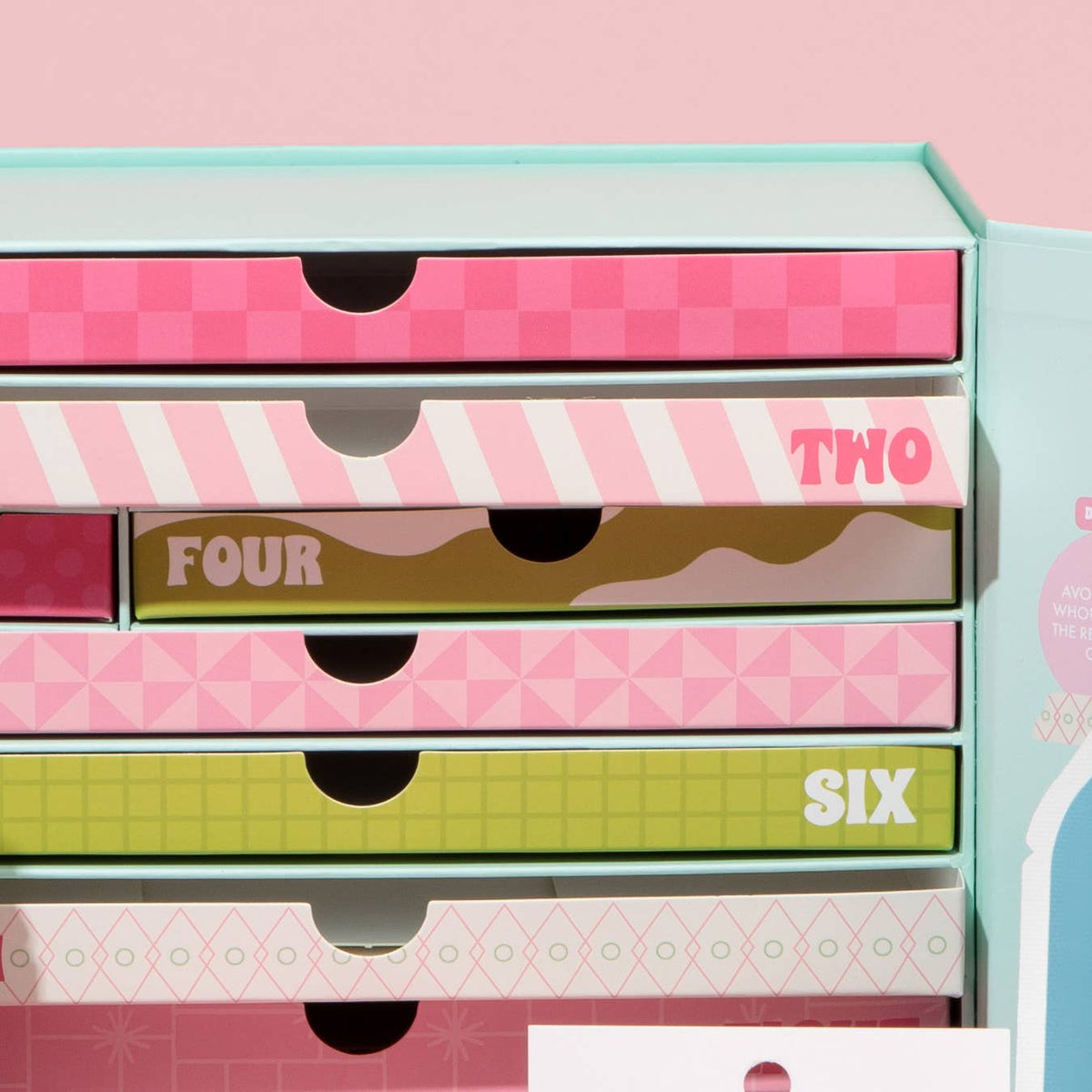 A pastel-colored drawer organizer box with six stacked drawers, each featuring a unique pattern and color scheme, including pink, white, olive green, and light blue. The drawers are labeled with numbers two through six.