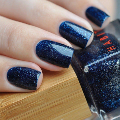 Nails with blue glitter polish and a bottle of Habibi nail polish.