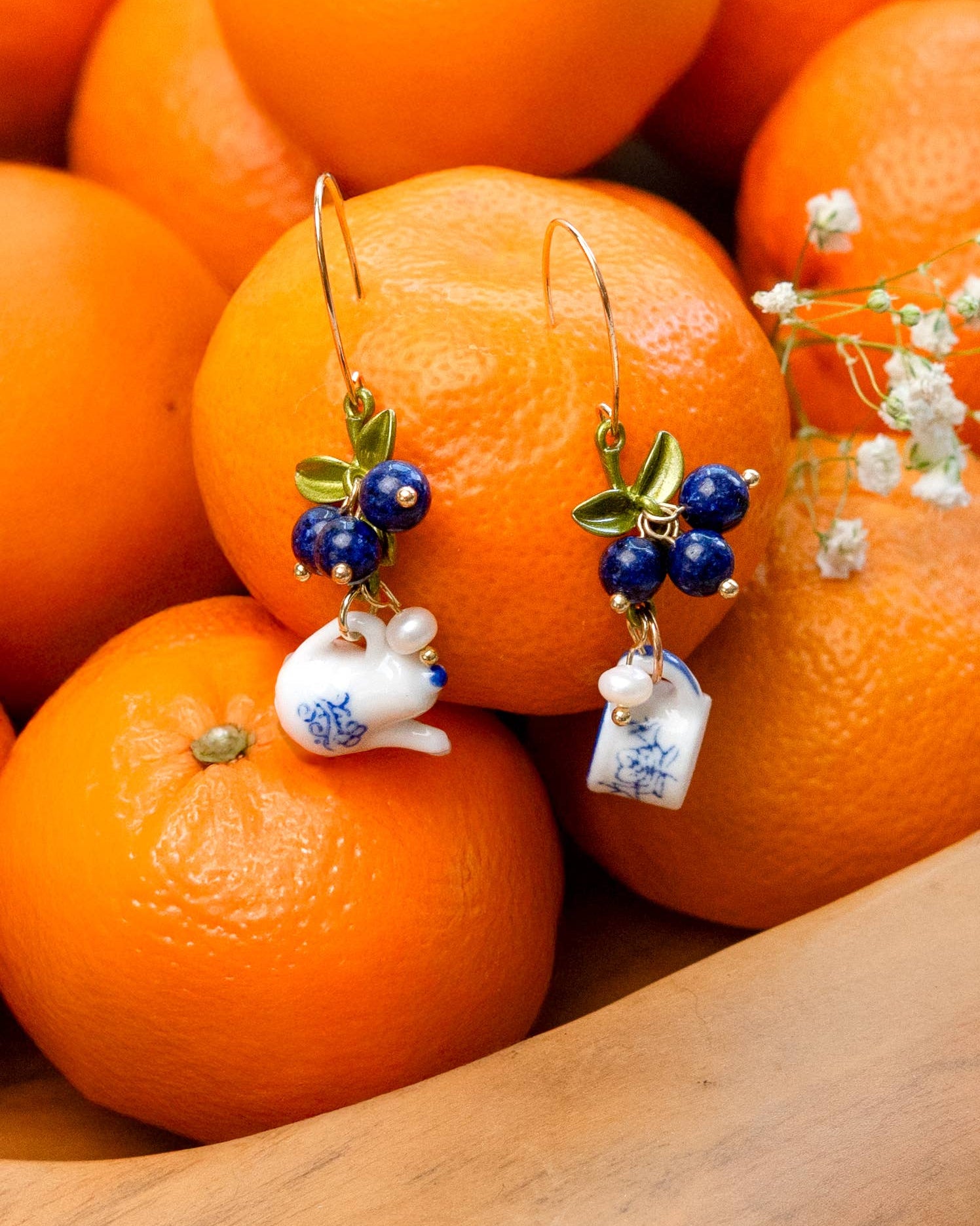 Earrings with ceramic rabbit charms on a pile of oranges, Spill the Tea Earrings