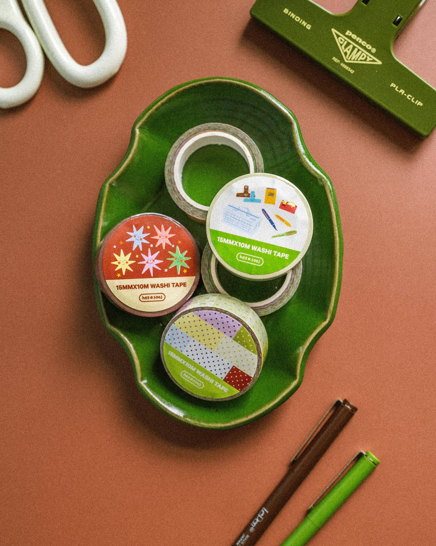 Assorted tape rolls on a green tray with scissors and a paper trimmer on a brown background