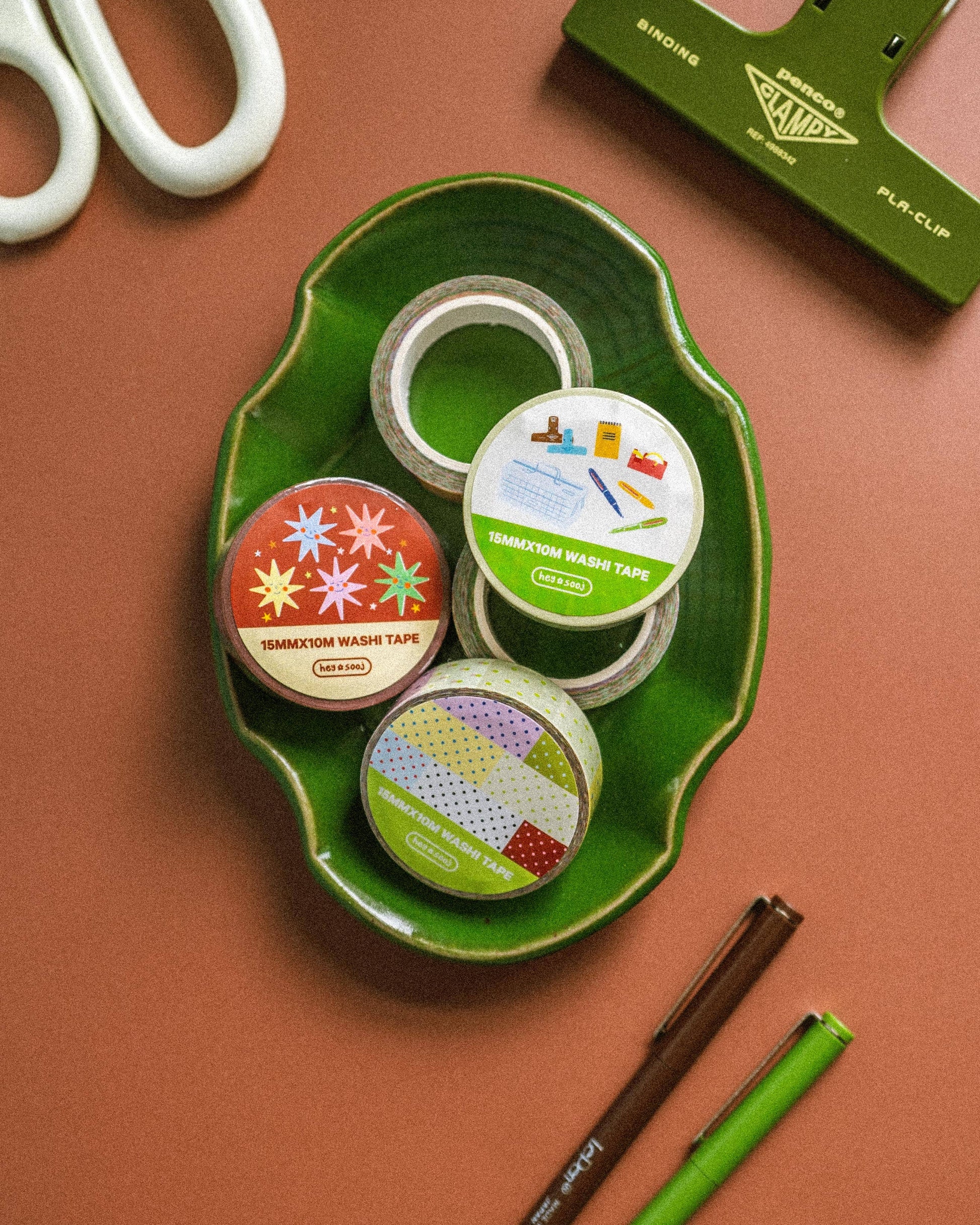 Assorted tape rolls on a green tray with scissors and a paper trimmer on a brown background