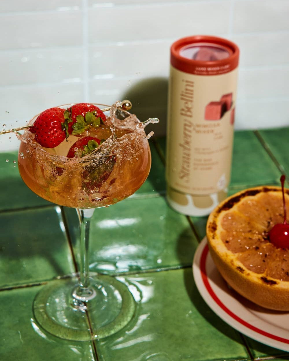 Cocktail with strawberries in a glass, and grapefruit with a cherry on a green tile surface, Strawberry Bellini Mixer