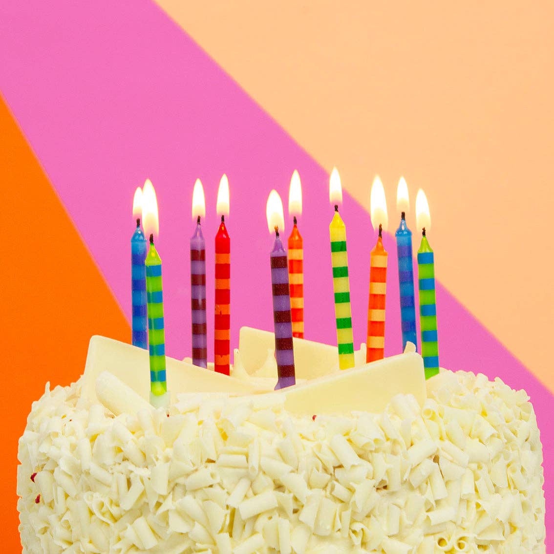 Birthday cake with colorful candles on a pink and orange geometric background