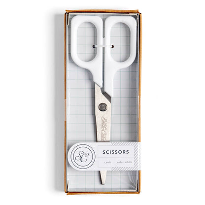White-handled scissors in a clear-front gift box with a white paper label that reads 'SCISSORS' and shows a monogram logo.