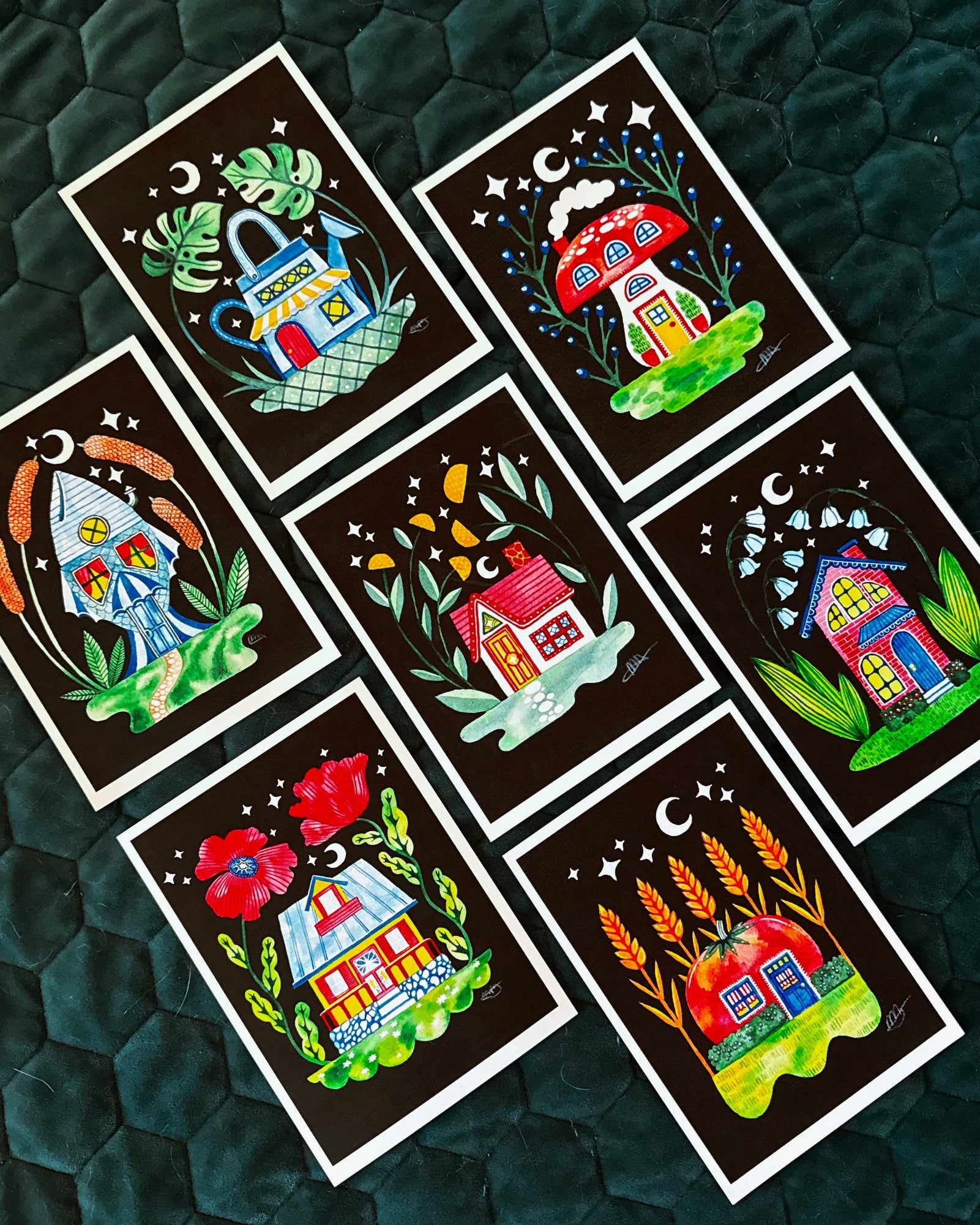Set of colorful house illustrations on black backgrounds arranged on a textured green surface.