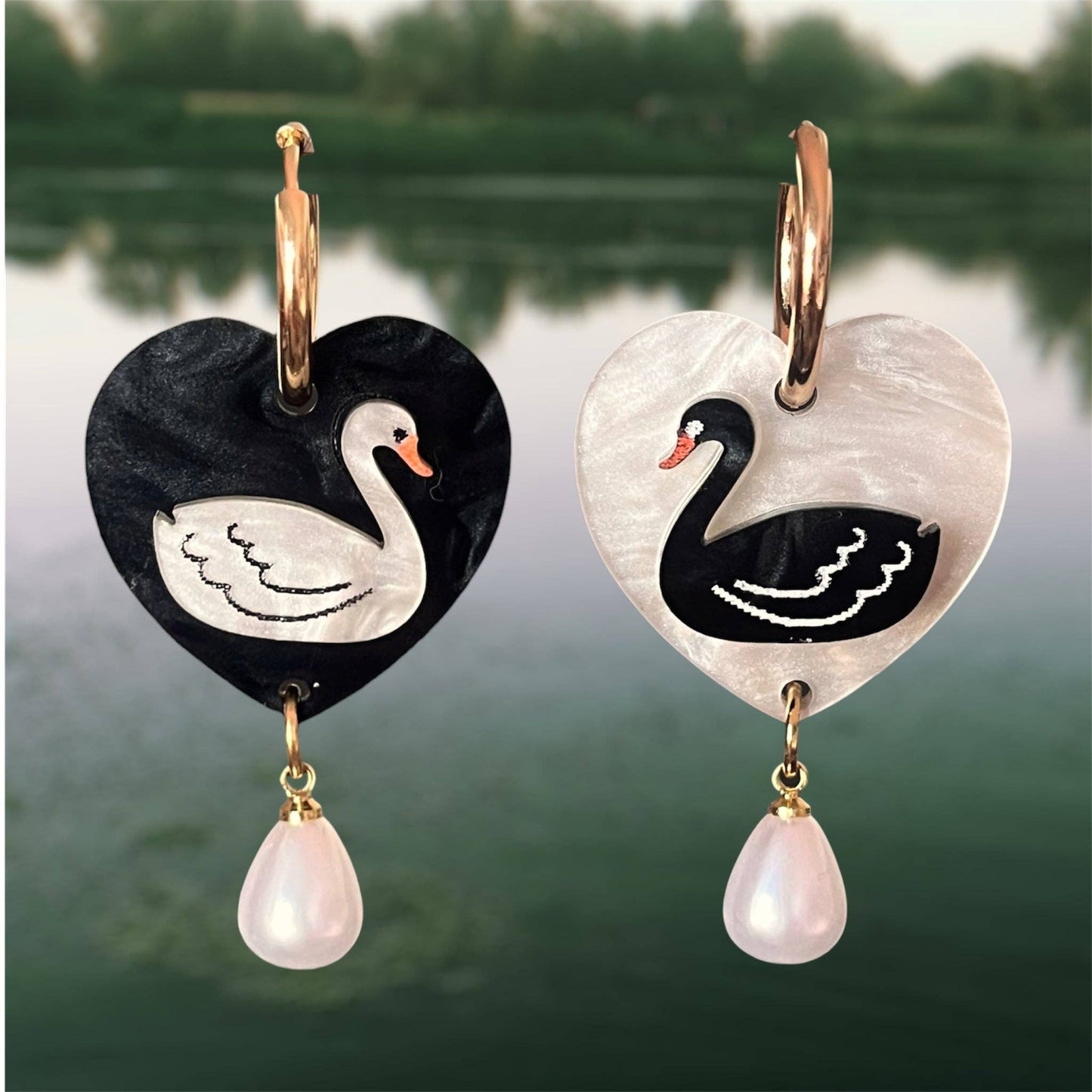 Heart-shaped earrings with swan designs and pearl drops against a blurred natural background