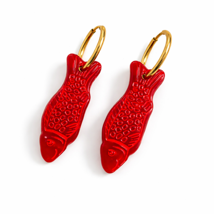 Red fish-shaped earrings with gold hooks on a white background