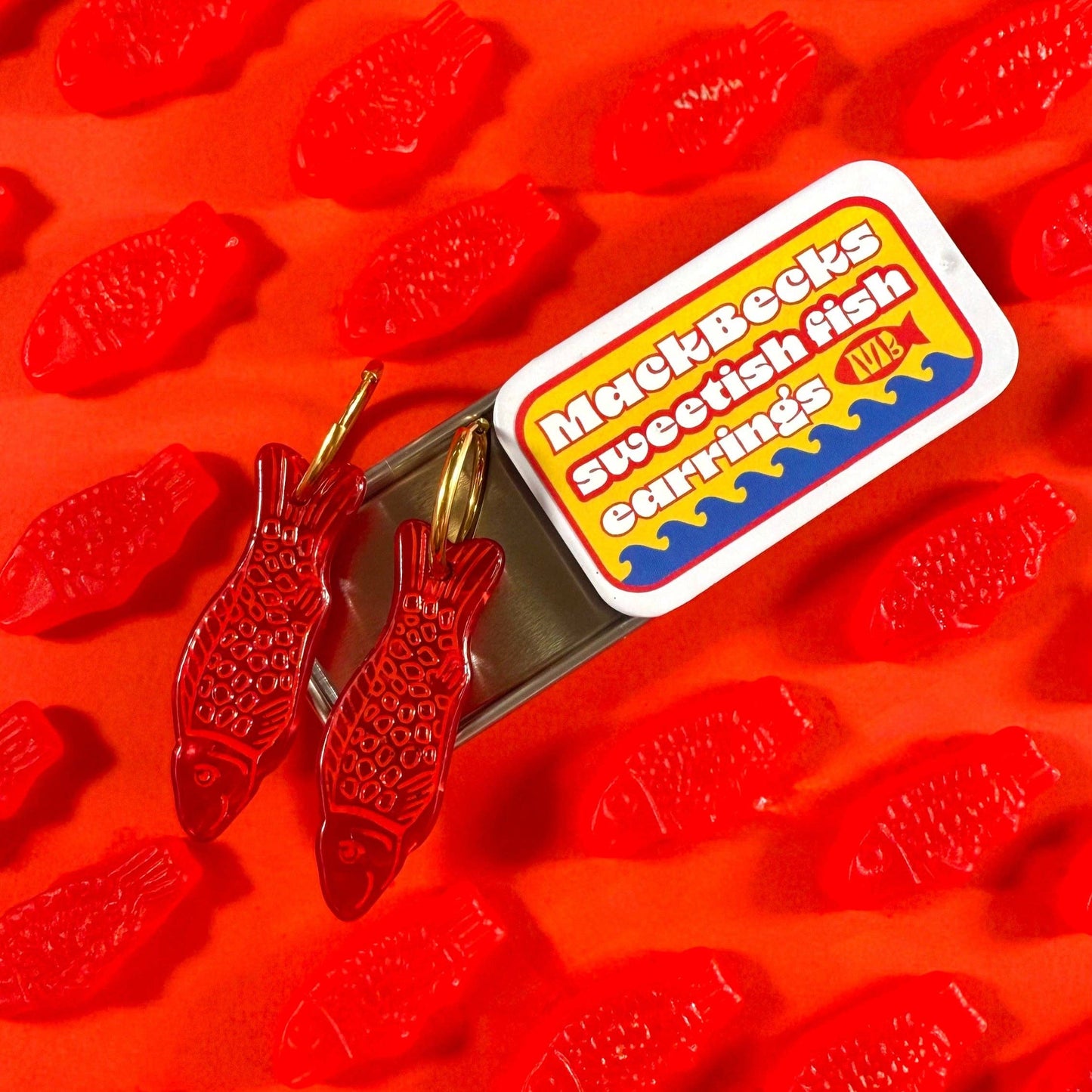 Red fish-shaped candies with a MackBecks Swedish Fish Earrings label on an orange background.
