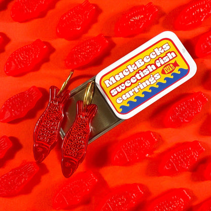 Red fish-shaped candies with a MackBecks Swedish Fish Earrings label on an orange background.