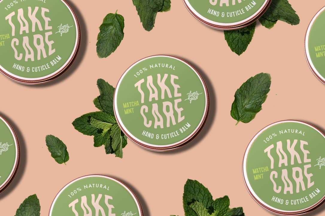 Green containers of 'Take Care' hand and cuticle balm with mint leaves on a beige background