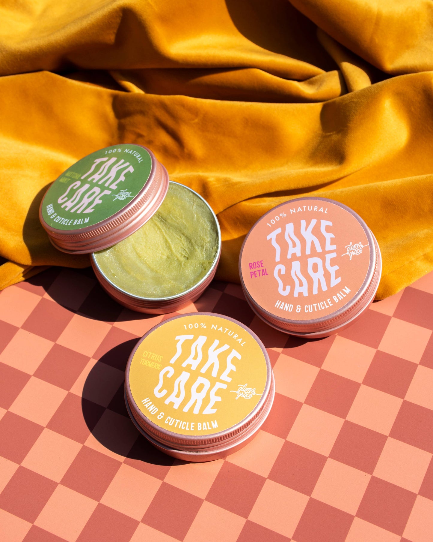 Three small containers labeled 'Take Care' on a checkered surface with a yellow fabric background.