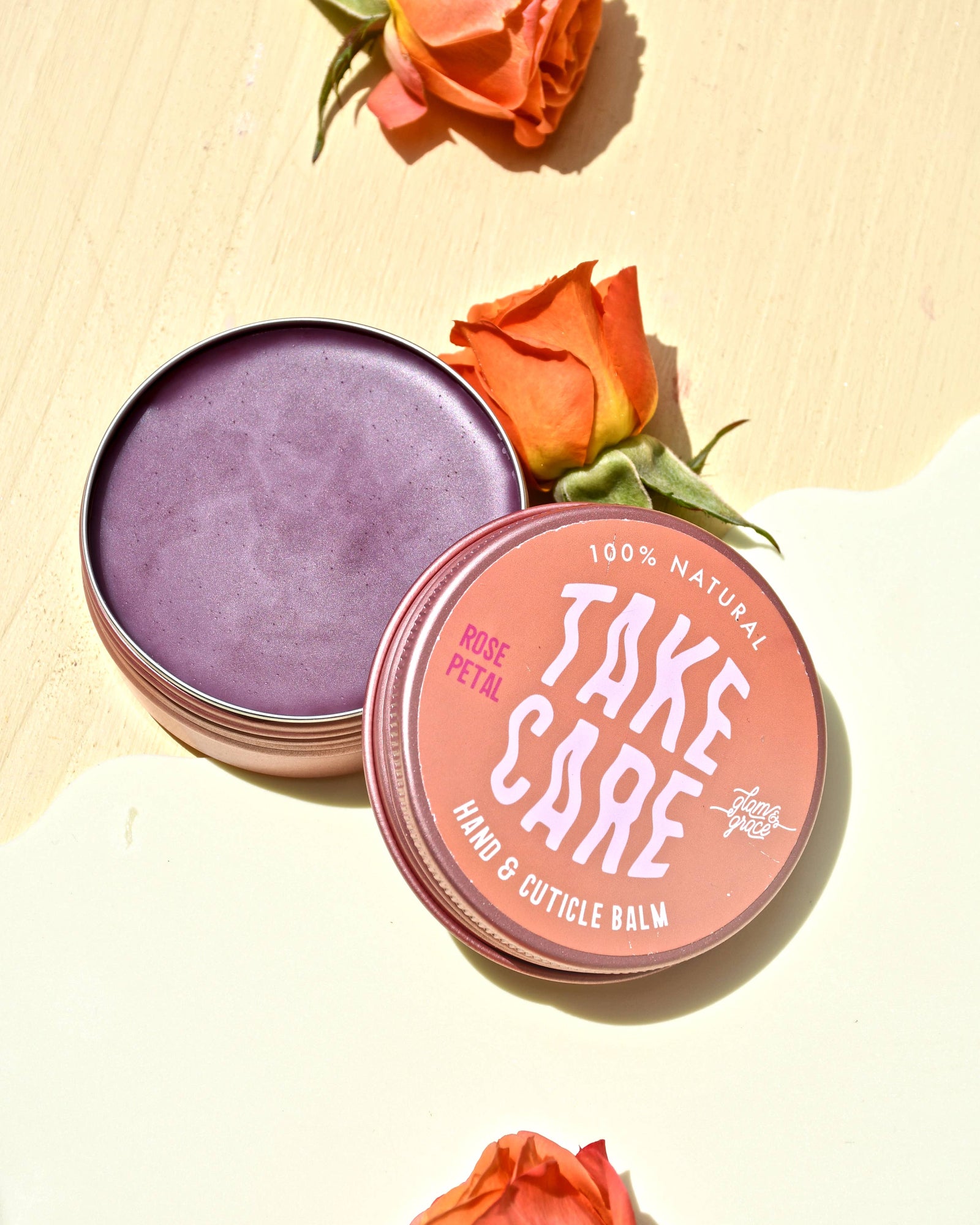 Hand and cuticle balm with 'Take Care' branding surrounded by orange roses on a light background