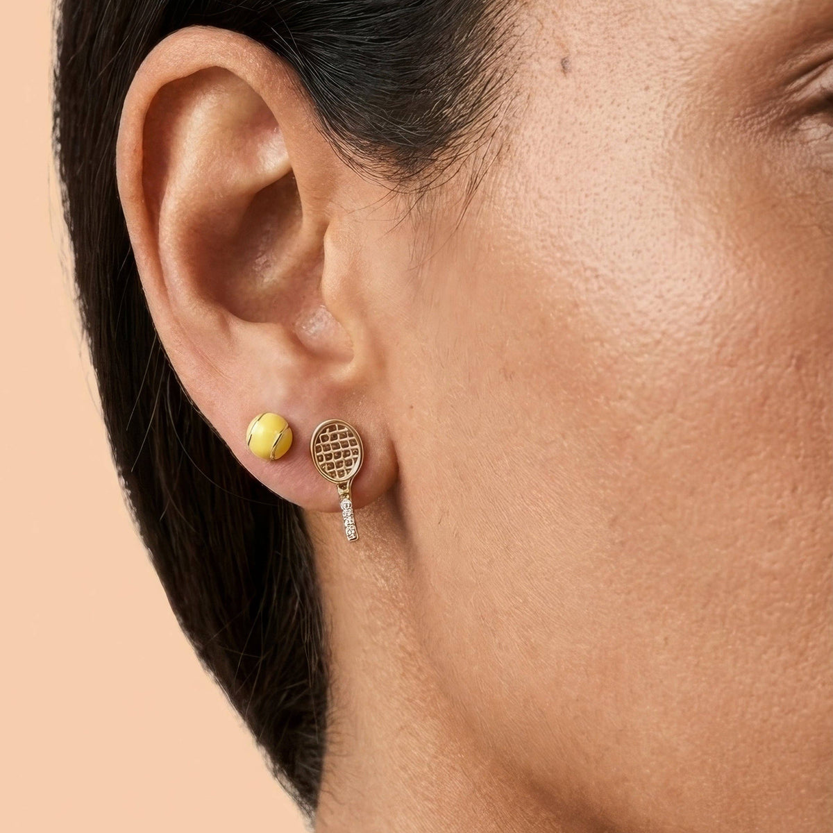 Close-up of a person wearing two earrings on a beige background