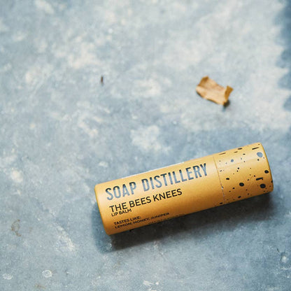 Lip balm container labeled 'The Bees Knees' from Soap Distillery on a textured surface.