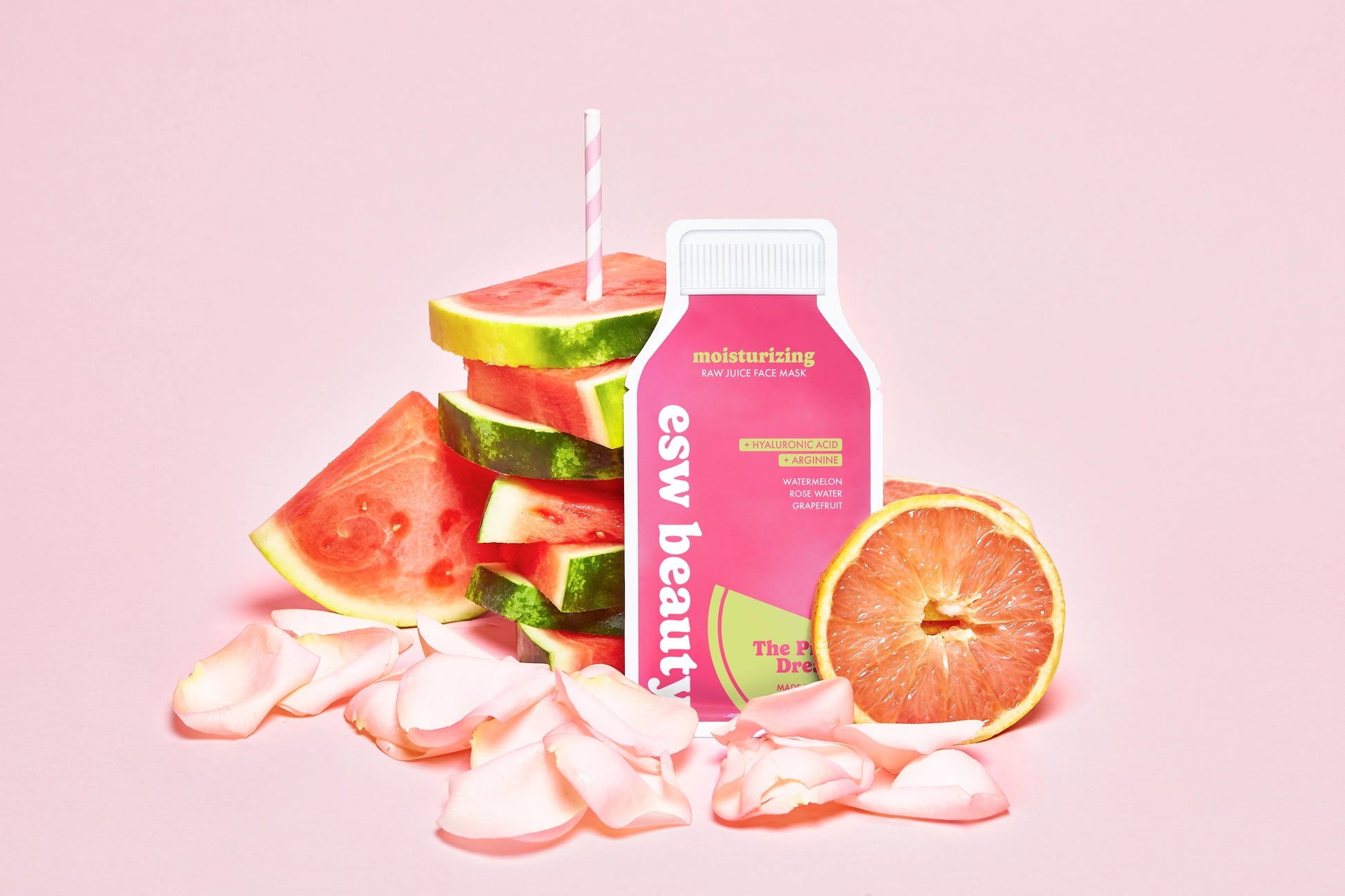 Pink bottle labeled 'esw beauty' with watermelon slices and a grapefruit on a pink background