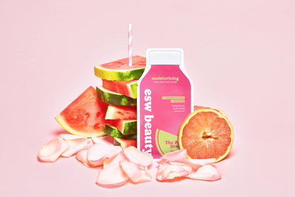 Pink bottle labeled 'esw beauty' with watermelon slices and a grapefruit on a pink background