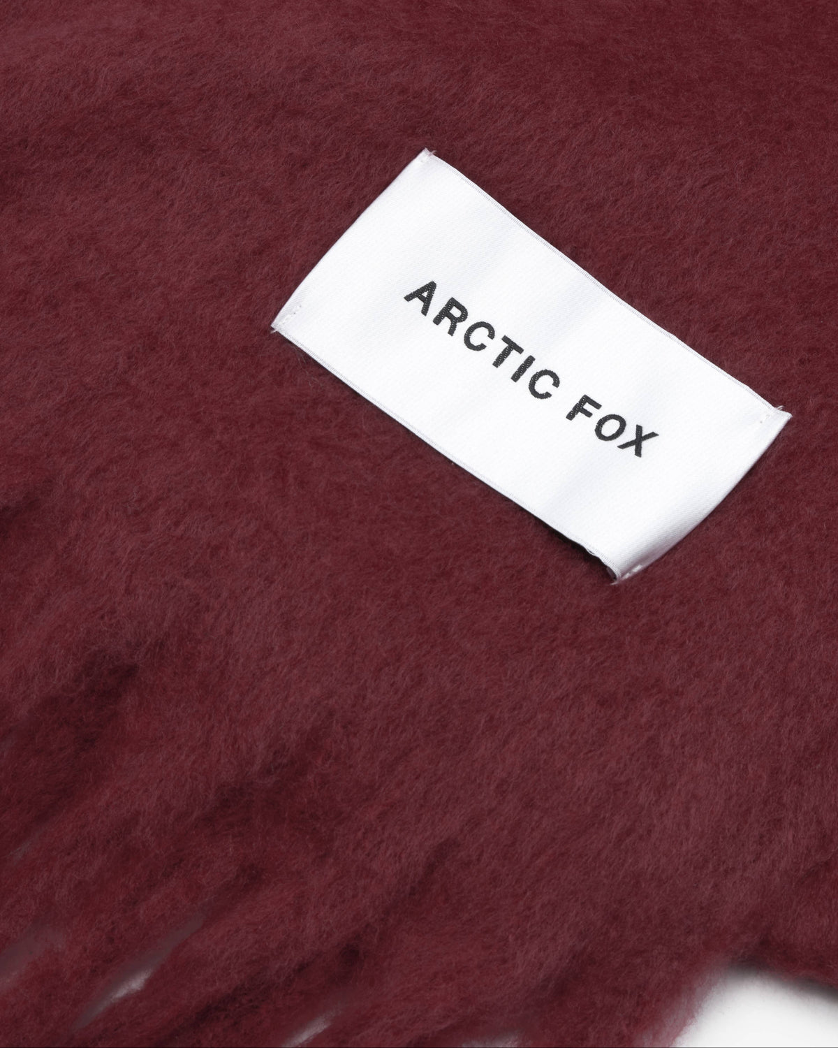 A close-up of a soft, fuzzy burgundy scarf with a white woven label reading 'ARCTIC FOX'.