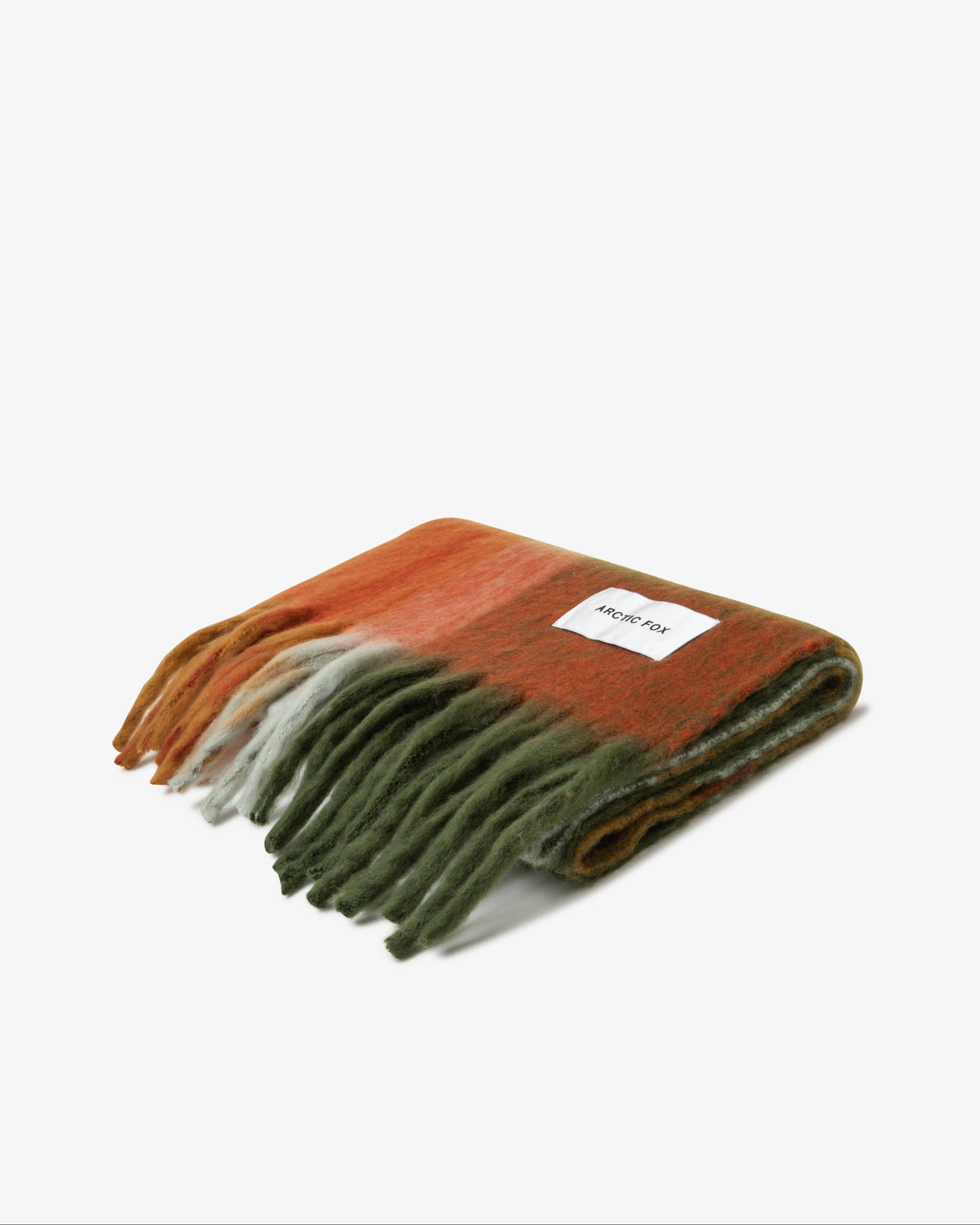 A folded wool scarf with fringe, featuring a color-blocked pattern of rust orange, dark brown, olive green, and off-white. A small white label with the brand name 'moulin roty' is visible on the rust-orange section.