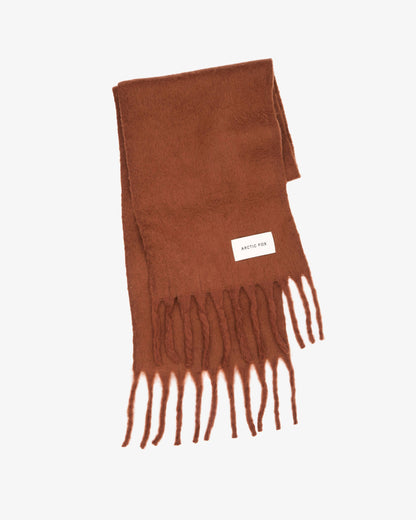 A rust-brown knit scarf with fringed ends and a small white rectangular brand label, photographed on a clean white background.