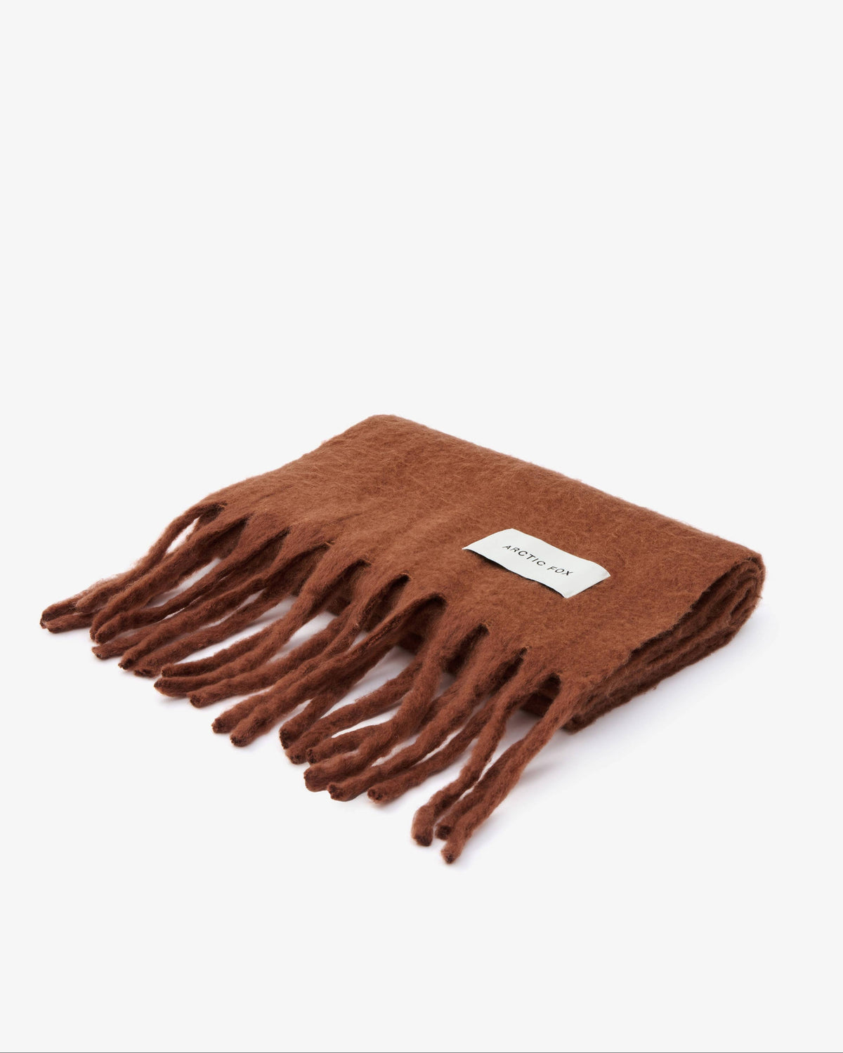 A folded brown knit scarf with fringed ends and a small white rectangular brand label, photographed on a clean white background.