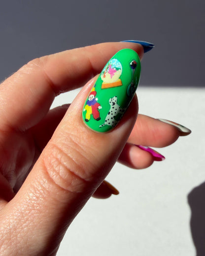 Hand holding a green nail with a cartoon design against a neutral background