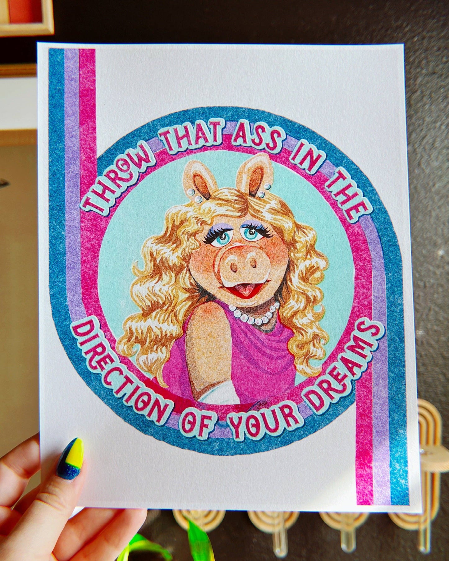 Cartoon character with text on a colorful background held by a hand.