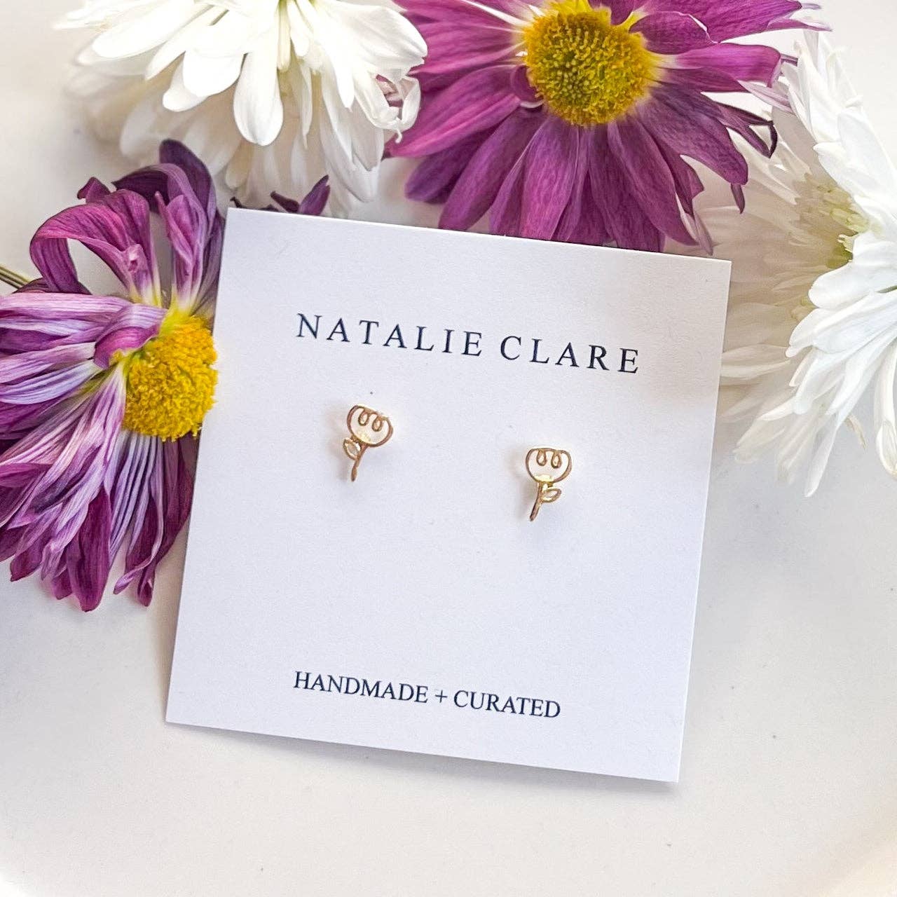 Gold earrings on a 'Natalie Clare' card with flowers around