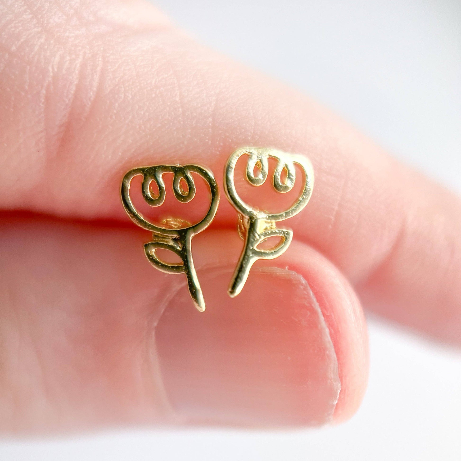 Gold earrings held between fingers on a light background