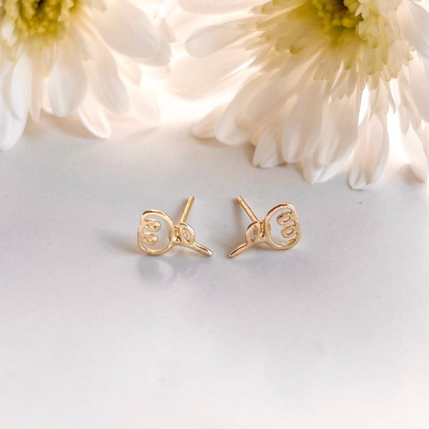 Gold heart-shaped earrings on a light surface with flowers in the background