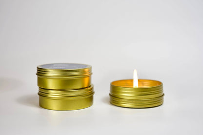 Two gold tins, one with a lit candle inside, on a white background