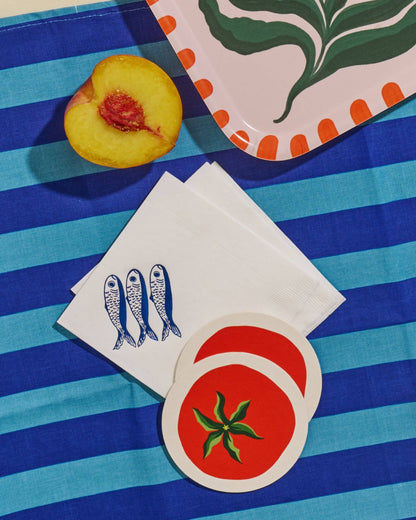 Stack of white sardine napkins, tomato coasters, and peach on a blue and white striped surface.